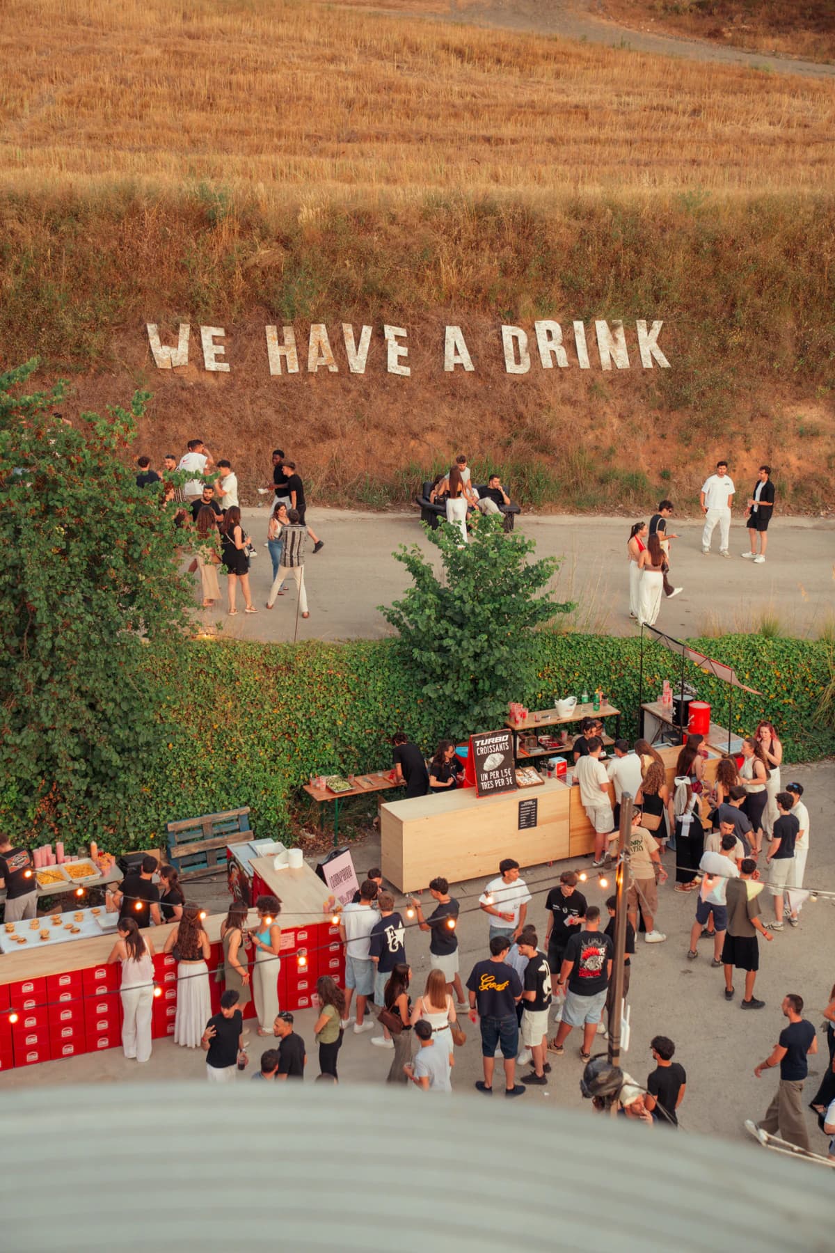 Aerial view of La Referència del Penedès’ Turbo Tarda, with hundreds of people in the courtyard and the We Have a Drink sign on the hill